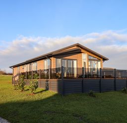 A single story wooden house with glass balcony panels surrounded by grass at Holly Lodge in Whitby