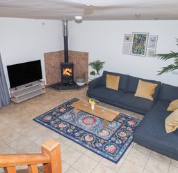 A living room with a dark gray sectional sofa and mustard pillows a wooden coffee table on a blue patterned rug a wood burning stove and a flat screen tv at The Old Coach House Little Dunley Cottages near Bovey Tracey
