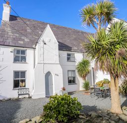A white house with slate roof and gravel yard with chairs and table at School House in Aberffraw