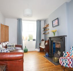 A living room with a leather sofa a colorful chair and a fireplace at School House in Aberffraw