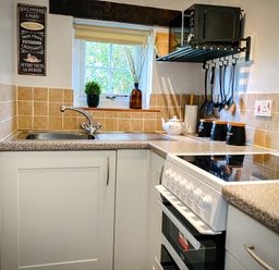 A kitchen sink with utensils hanging and a stove next to a window at Hawthorn Crackington near Crackington Haven