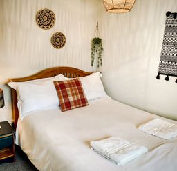 A bedroom with a wooden bed white bedding a checked pillow two folded towels a bedside table with a lamp and wall decorations at Hawthorn Crackington near Crackington Haven