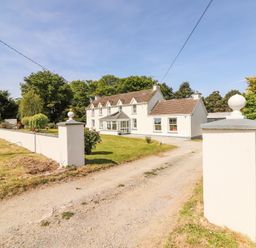 A farmhouse with a gravel driveway and white boundary wall surrounded by trees and grass at Dromclough Farmhouse in Dromclough near Listowel County Kerry