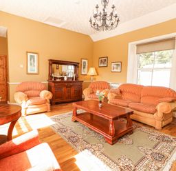 A living room with orange striped sofas a wooden coffee table and sideboard a patterned rug and a chandelier at Dromclough Farmhouse in Dromclough near Listowel County Kerry