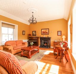 A living room with sofas, a fireplace, a piano, a coffee table, paintings on walls, and wooden flooring at Dromclough Farmhouse in Dromclough near Listowel County Kerry