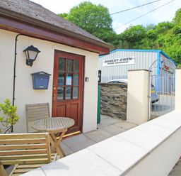 An outdoor patio area with wooden chairs and table by a brown door next to a white wall and gate at Fisherman Cove in Porthmadog