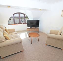 A living room with two beige sofas a round wooden coffee table a flat screen tv on a wooden stand and a window with a view of water at Fisherman Cove in Porthmadog