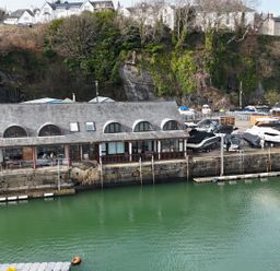 A waterfront building with boats docked and parked on the shore at Fisherman Cove in Porthmadog