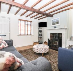 A living room with wooden ceiling beams fireplace patterned ottoman and two sofas at Chestnut Cottage in Wetwang near Great Driffield