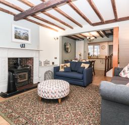 A living room with a fireplace blue sofas a patterned ottoman and a dining area in the background at Chestnut Cottage in Wetwang near Great Driffield