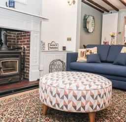 A living room with a blue sofa decorated with cushions a round patterned ottoman and a fireplace at Chestnut Cottage in Wetwang near Great Driffield