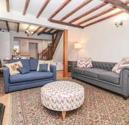 A living room with two sofas one blue and one gray and a round patterned ottoman at Chestnut Cottage in Wetwang near Great Driffield