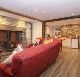 A living room with a red sofa facing a stone fireplace with a wood stove and an open kitchen with wooden countertops at Miners Rest in Blaenau Ffestiniog