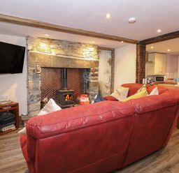 A living room with a red sofa facing a stone fireplace with a wood-burning stove and a wall-mounted TV at Miners Rest in Blaenau Ffestiniog