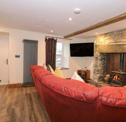 A living room with a red sofa a stone fireplace with wood burner and a wall-mounted TV at Miners Rest in Blaenau Ffestiniog