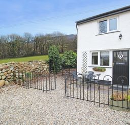 A gravel courtyard with black metal chairs and table outside a white house with a black door at Dowlais in Llanllyfni near Penygroes
