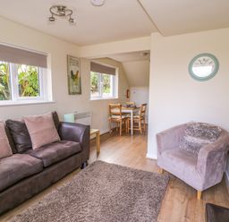 A living room with a brown sofa and armchair a clock on the wall and a dining table with chairs in Dowlais Llanllyfni near Penygroes