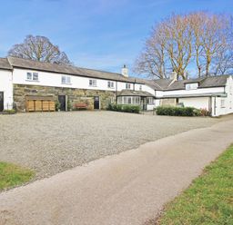 A gravel driveway in front of a long two story house with stone and white walls and leafless trees in the background at Igamogam Llanllyfni near Penygroes