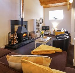 A living room with a wood-burning stove sofa chairs coffee table and television at Igamogam in Llanllyfni near Penygroes