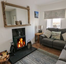 A living room with a lit fireplace a large mirror two gray sofas and a wooden side table at Camwy in Brynsiencyn