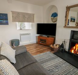 A living room with a gray sofa cushions a patterned rug fireplace and a wooden tv stand at Camwy in Brynsiencyn