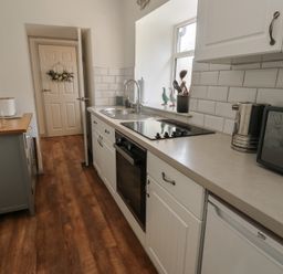 A kitchen with white cabinets a countertop stove a sink a microwave electric kettle and wooden flooring at Camwy in Brynsiencyn