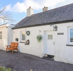 A white house exterior with a black slate roof wooden bench hanging plant and a small welcome sign at Camwy in Brynsiencyn