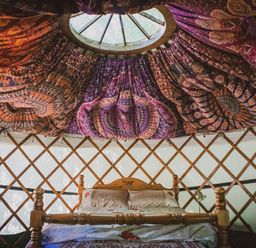 A wooden bed with pillows and bedding under a colorful fabric ceiling in a yurt at Brandon House Farm Yurt Brandon Parva near Mattishall