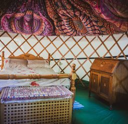 A wooden bed with a patterned cover and a wooden chest at the foot inside a yurt with patterned fabric on the ceiling and a wooden cabinet Brandon House Farm Yurt Brandon Parva near Mattishall