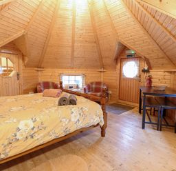 A wooden interior bedroom with a bed with floral bedding two armchairs a table with benches and wooden walls at Enchanted Cottage in Snettisham