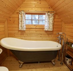 A bathroom with a clawfoot bathtub a small window with curtains wooden walls and floor at Enchanted Cottage in Snettisham