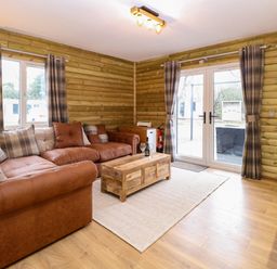 A living room with brown leather sofas a wooden coffee table and checkered curtains at Rabbit Warren Lodge in Snettisham