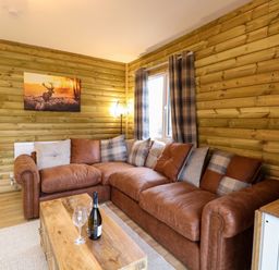 A living room with a brown leather sofa and plaid cushions beside a window with plaid curtains at Rabbit Warren Lodge in Snettisham