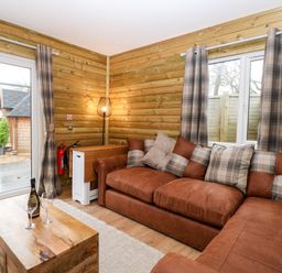 A living room with a brown sectional sofa with plaid cushions near wood paneled walls at Robins Nest Lodge in Snettisham