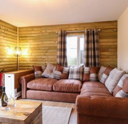 A corner sofa with cushions in a wooden paneled room with a wooden table and wine glasses at Robins Nest Lodge in Snettisham