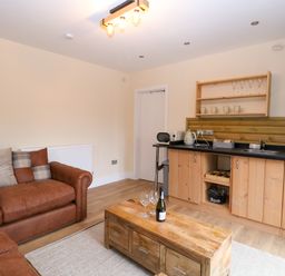 A living area with a brown sofa wooden coffee table and a kitchenette with wooden cabinets at Robins Nest Lodge in Snettisham