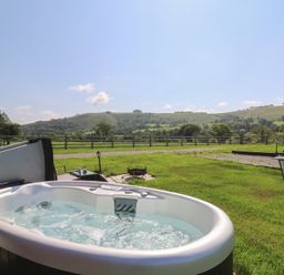 A hot tub on grass with a view of hills at Ty Twt Teifi in Tregaron