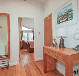 A hallway with wooden floor a large mirror a wooden table with a lamp and decorations a door and a view into a living room at 1 Miller's Island near Lanreath