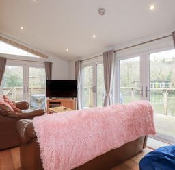 A living room with brown leather sofas covered with pink throws a wooden coffee table a television and glass doors with curtains at 1 Miller's Island near Lanreath