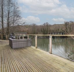 A wooden deck with outdoor seating overlooking a lake and trees at 1 Millers Island near Lanreath