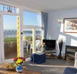 A living room with a glass door and windows overlooking the sea at Homestead in Aberdesach near Penygroes