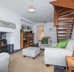 A living room with armchairs a fireplace a wooden staircase a bookshelf and a lamp at Quarrymans cottage in Beddgelert