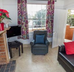 A living room with a blue armchair a black sofa with a red cushion a fireplace a small black table with a television and floral curtains at 1 Willow Cottage in Upton Upon Severn