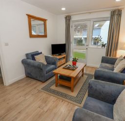 A living room with blue armchairs a wooden coffee table a television on a stand and curtains at Pierpont D1 Norton near Yarmouth