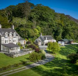 A stone house with multiple chimneys and an adjoining building surrounded by trees and lawn at Tan Llan in Llanelltyd near Dolgellau