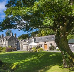 A large stone house with chimneys and windows surrounded by grass and trees at Tan Llan in Llanelltyd near Dolgellau