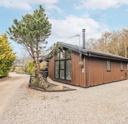 A brown building with windows and trees at Fig Tree Lodge, Hutton Roof near Penrith