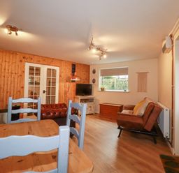 A living room with wooden dining table and chairs a leather sofa a TV on a stand and a wooden chest at The Aqua Shack in Newquay