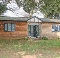 A wooden cottage with two windows and an open front door surrounded by trees at Holm Oaks Cottage in Busbridge near Godalming