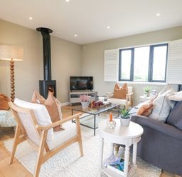 A living room with chairs a sofa a glass coffee table a floor lamp and a wood stove at Holm Oaks Cottage in Busbridge near Godalming